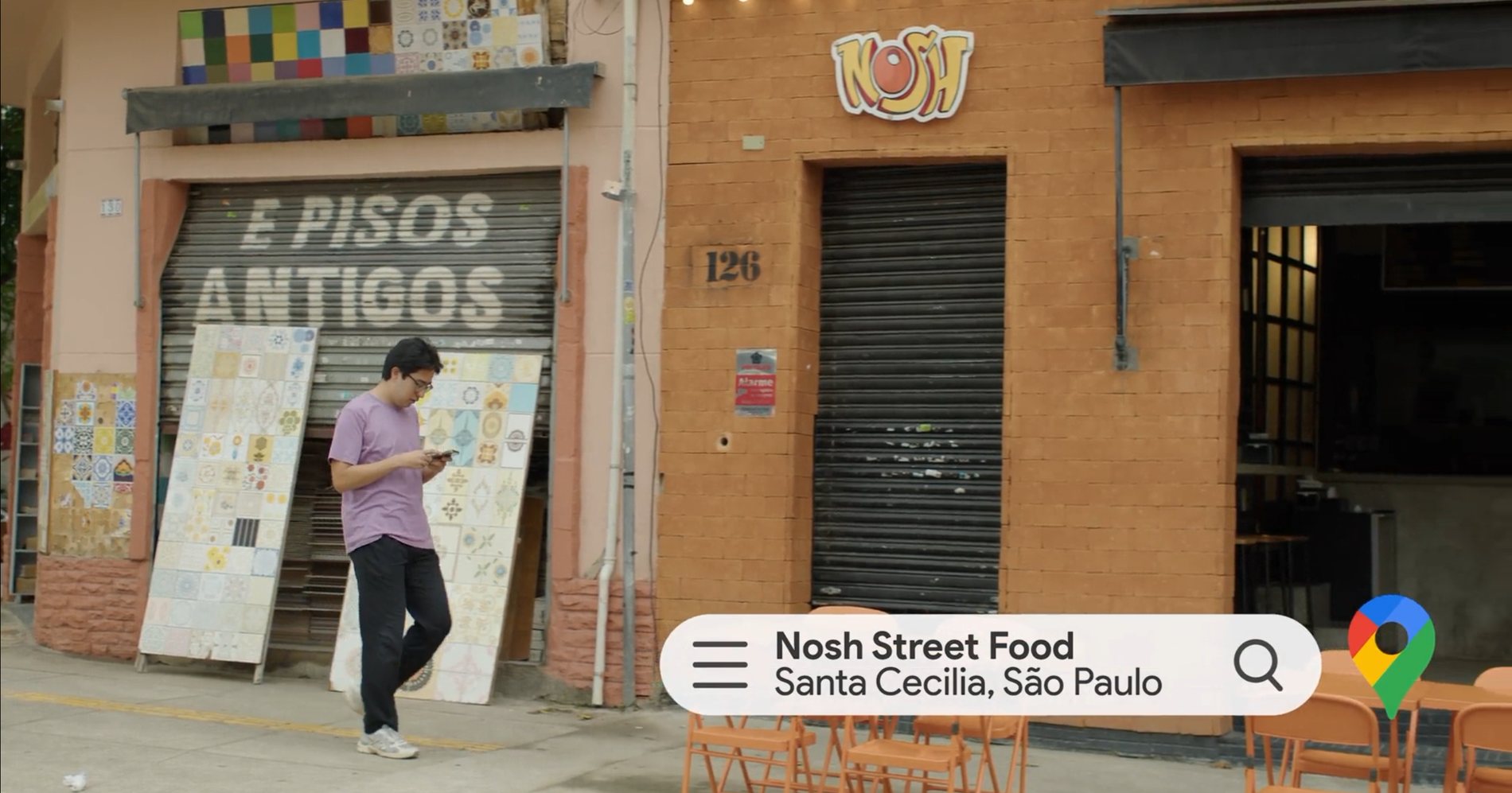 Rapaz caminhando diante de um restaurante em Santa Cecília, com a busca do Google Maps na tela