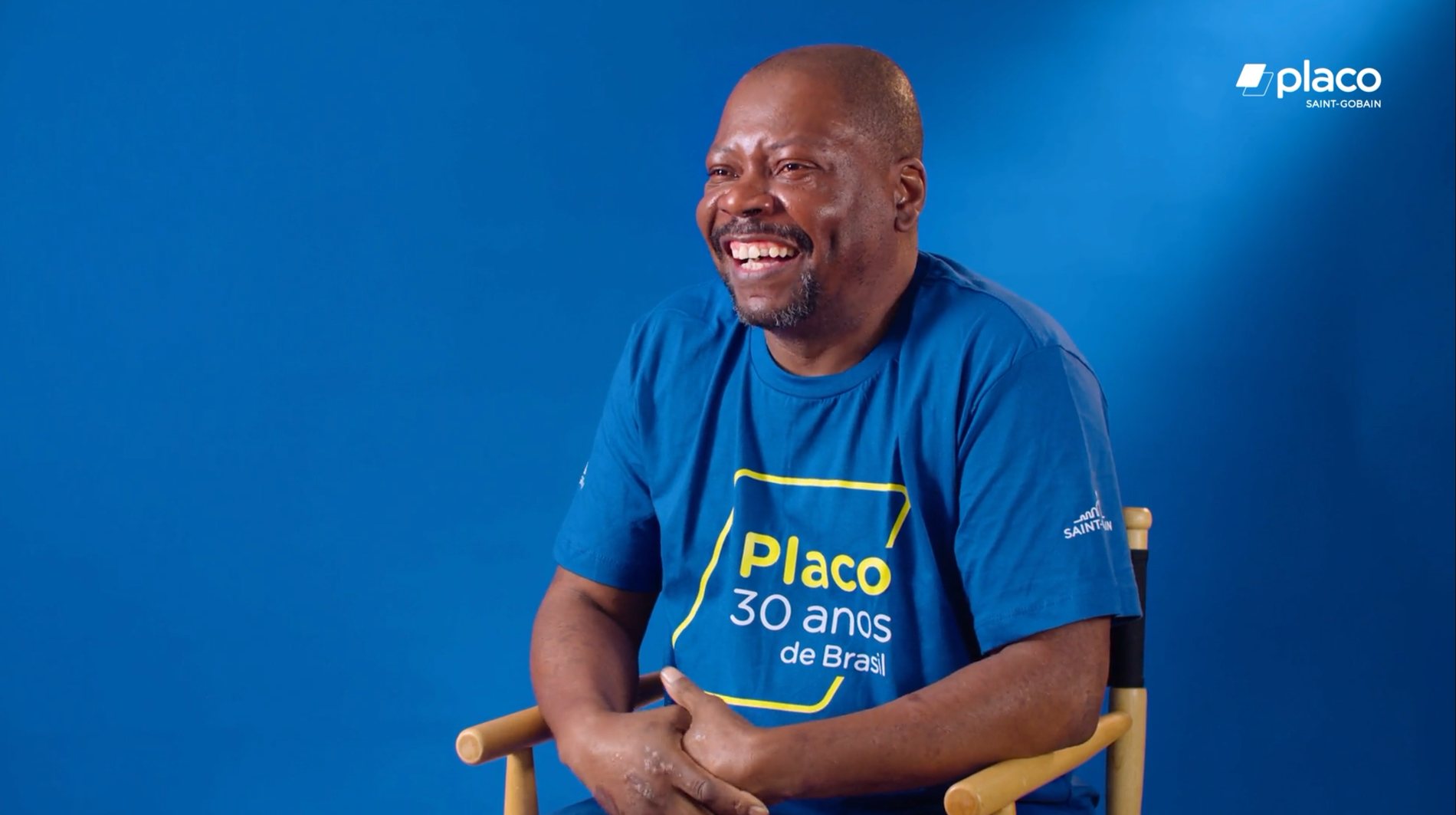 Entrevistado sorrindo diante de fundo azul, com camiseta Placo 30 anos